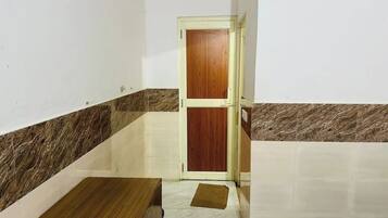 Une petite pièce avec une porte en bois, un sol carrelé de marbre et un tapis marron.