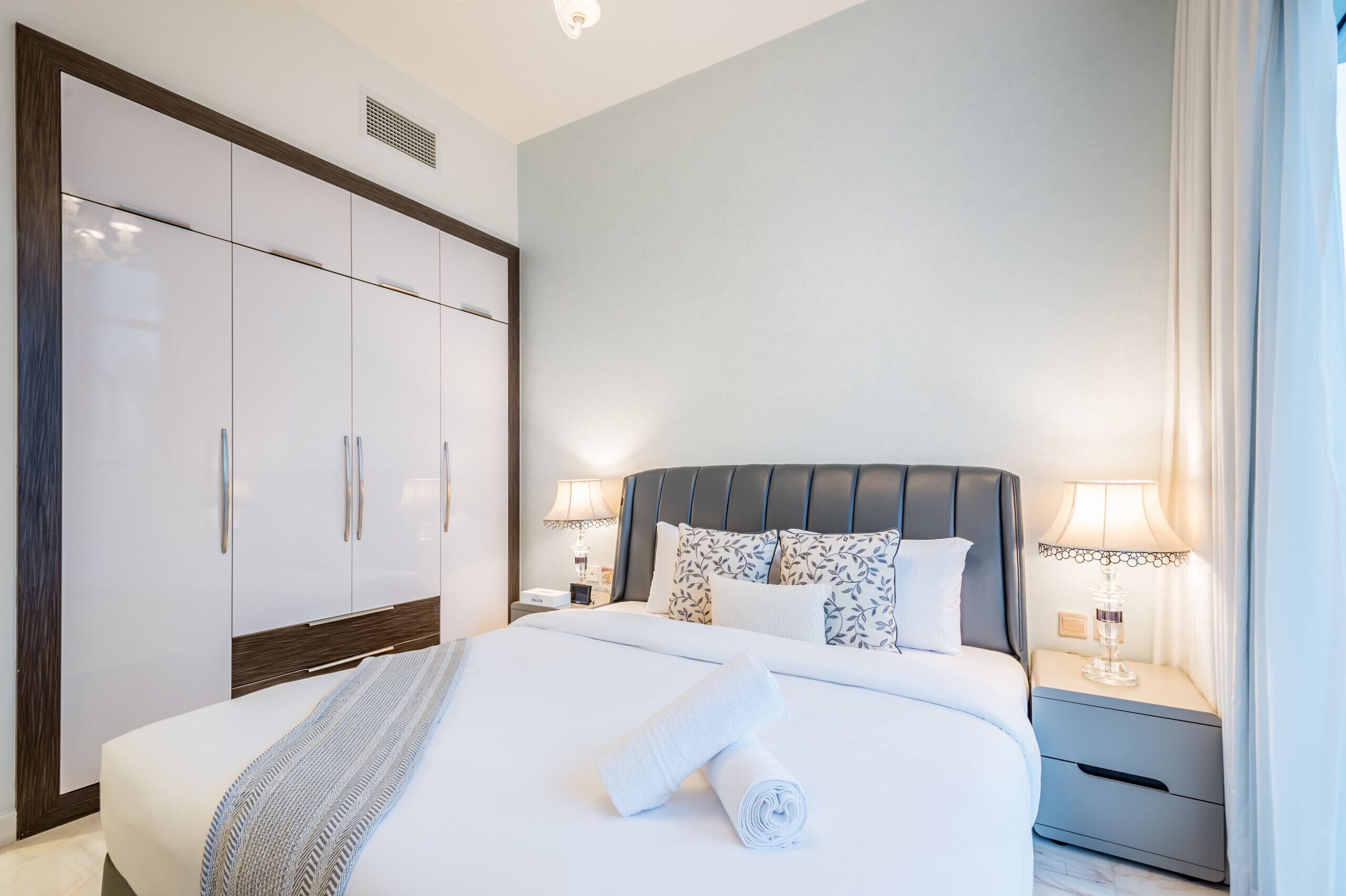 Una camera d'albergo con un letto grande, un armadio, due comodini con lampade e una finestra con tende.