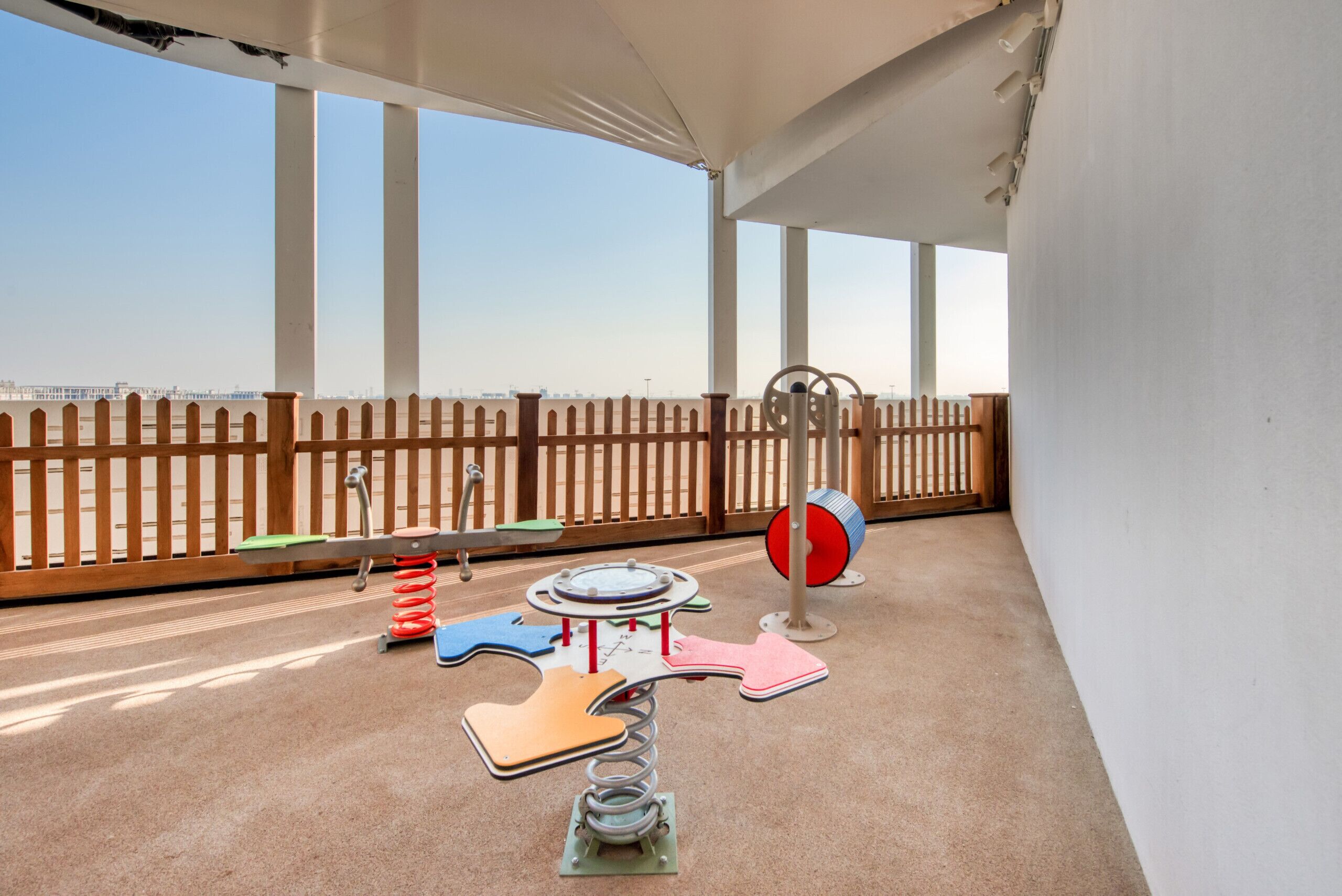 Zona de juegos infantiles con columpios, un sube y baja y una piscina de pelotas.