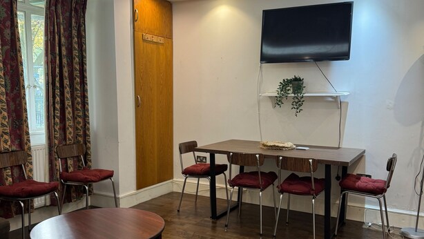 A dining area with a wooden table and six chairs, a television mounted on the wall, and a door with a wooden panel.