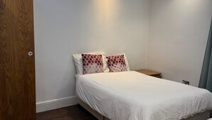 A modern bedroom with a wooden door, a bed with patterned pillows, a nightstand, and a marble table.