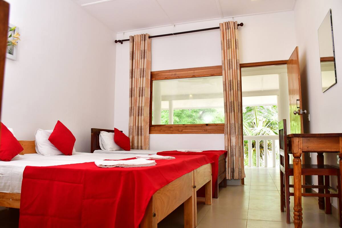 A hotel room with two beds, red bedding, a wooden desk, and a large window with curtains.