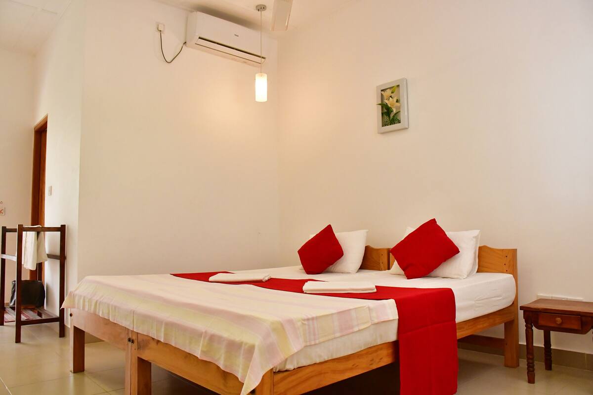 A neatly made bed with red and white bedding, a wooden headboard, and a small bedside table.
