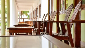 A corridor with wooden chairs and tables, suggesting a waiting area or lounge. - Sea Way Hotel (Nilaveli)