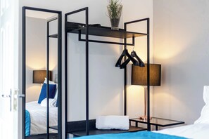 Una habitación de hotel con cama, mesita de noche, lámpara, espejo y perchero.