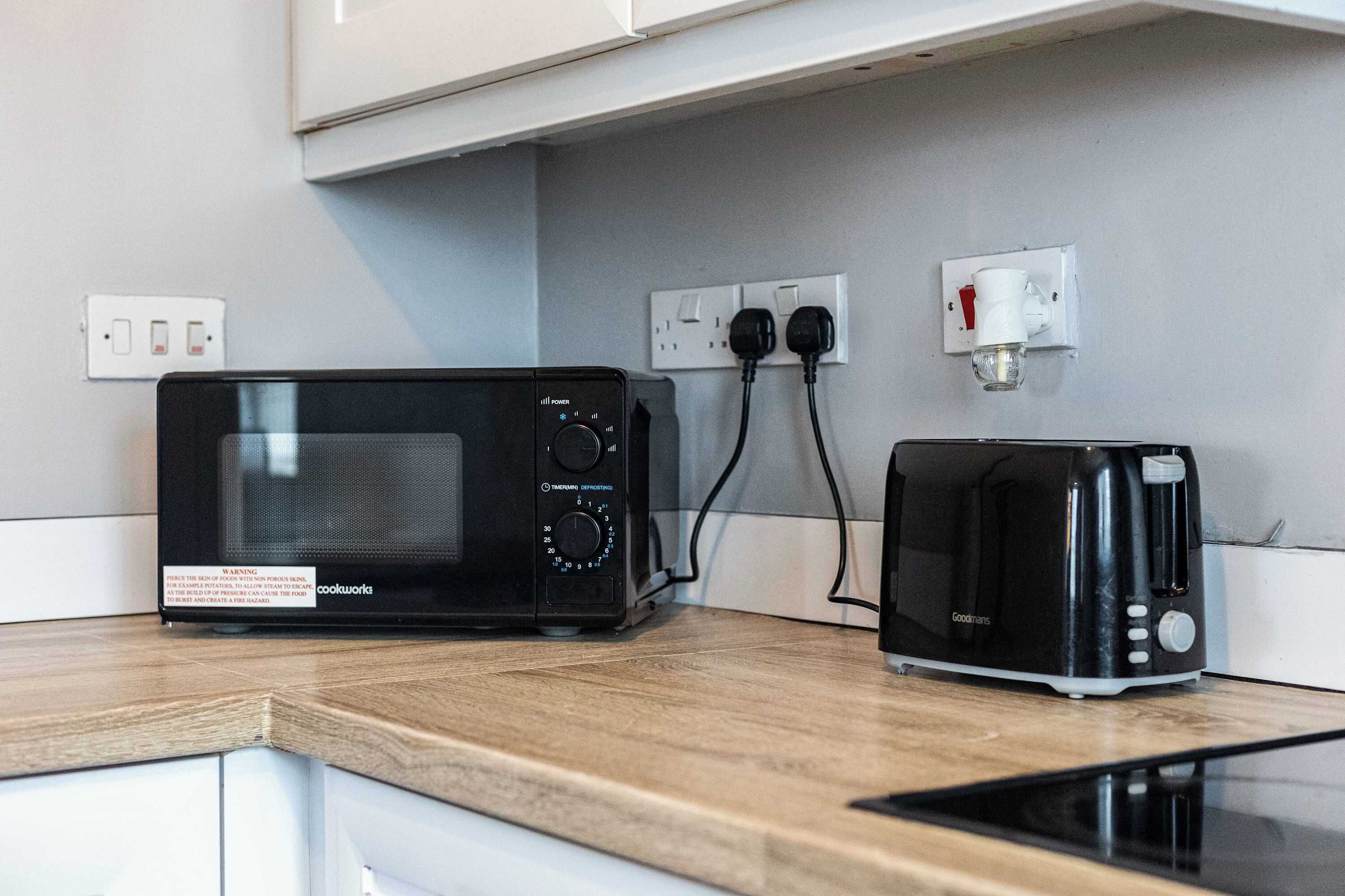 A kitchen with a microwave and toaster on a wooden countertop, connected to wall outlets.