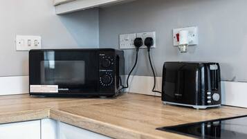 A kitchen with a microwave and toaster on a wooden countertop, connected to wall outlets.