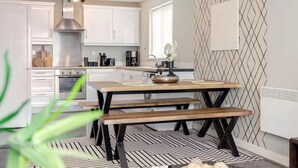 Une cuisine moderne avec des meubles blancs, une hotte en acier inoxydable et une table à manger en bois, accompagnée de bancs.