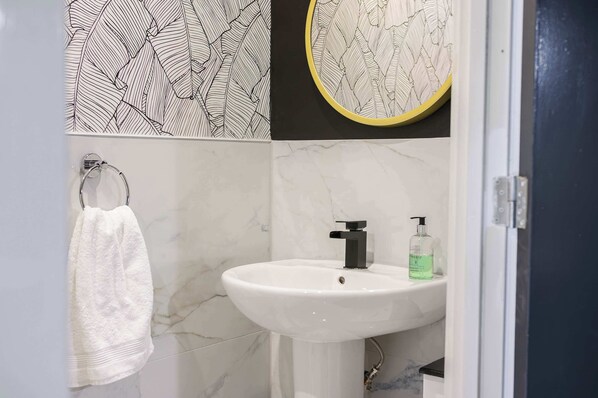A bathroom with a white sink, a towel rack, a mirror, and patterned wall tiles.