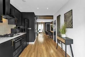 A modern kitchen with a central island, black cabinetry, and a wooden floor.