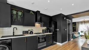 A modern kitchen with black cabinetry, a stainless steel range hood, a built-in microwave, and a dishwasher.