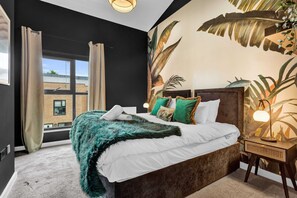 Relax in a stylish room with a large bed, tropical leaf mural, and a window offering a view of the outside.