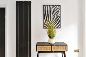 A modern room with a black and white striped wall panel, a framed abstract art piece, and a small table with a potted plant.