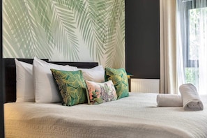 A neatly made bed with a white comforter and several pillows, including some with tropical leaf patterns.