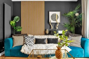 Un salon moderne avec un canapé de couleur turquoise, des coussins aux motifs noir et blanc, un plaid en fausse fourrure et un centre de table décoratif en forme d’ananas.
