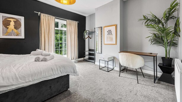 Un dormitorio con cama, escritorio, silla, planta en maceta y lámpara colgante.
