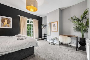 A bedroom with a bed, a desk, a chair, a potted plant, and a hanging light fixture.