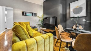 Una sala de estar moderna con un sofá amarillo, una mesa de comedor con sillas, un televisor de pantalla plana y una obra de arte enmarcada en la pared.