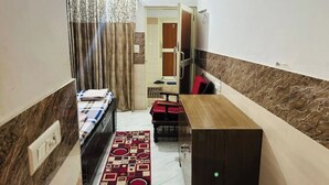 Ein schmales Hotelzimmer mit einem Bett, einem kleinen Tisch, einer roten Bank und einem Holzkasten.