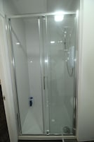 A glass-enclosed shower stall with a handheld showerhead and a handheld faucet.