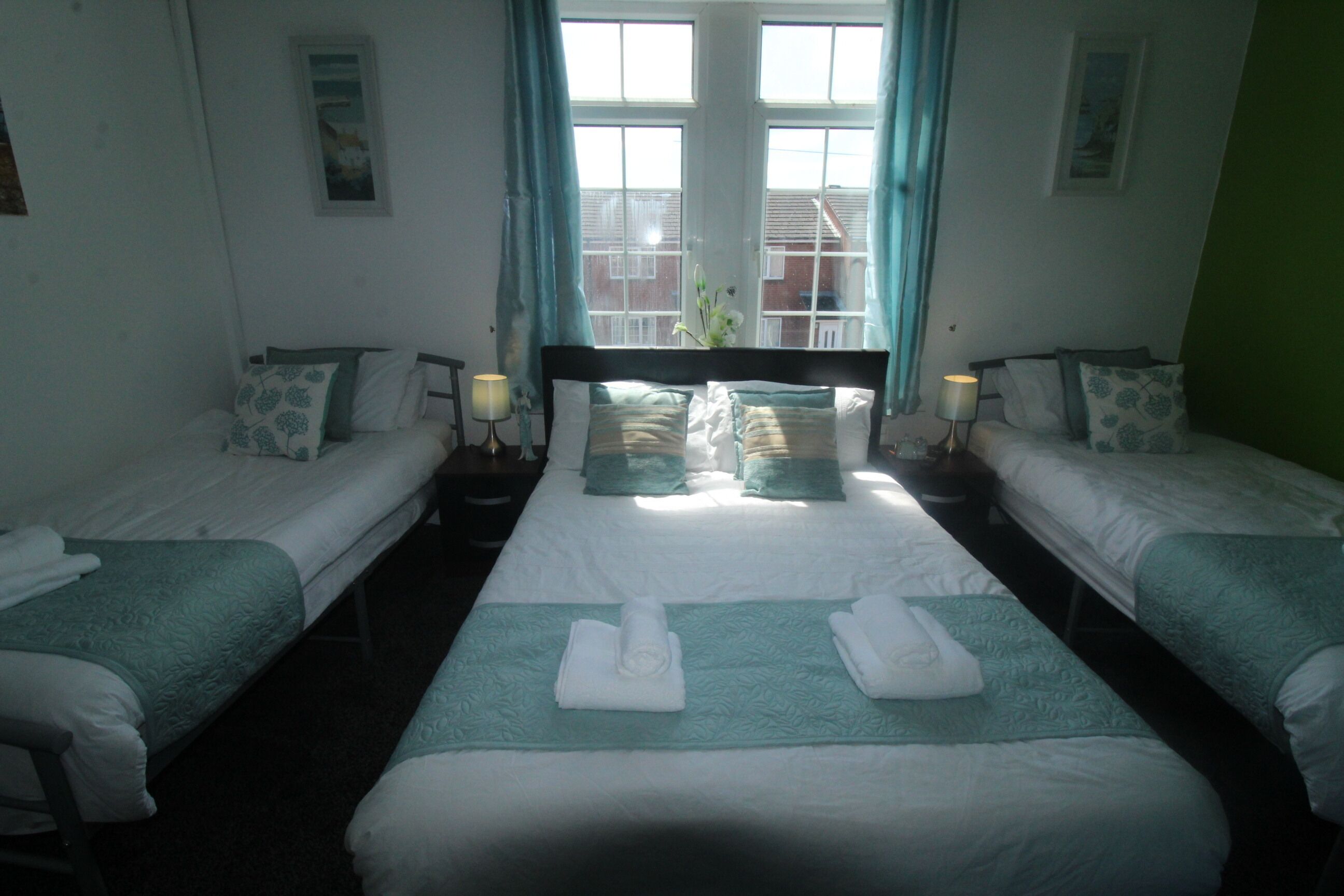 A hotel room with two single beds, a large bed, and a window with curtains.
