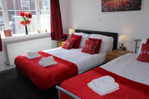 A hotel room with two beds, each with red bedding and white pillows, a radiator, a window with a view of the street, and a sign on the window. - High Street House (Rotherham)