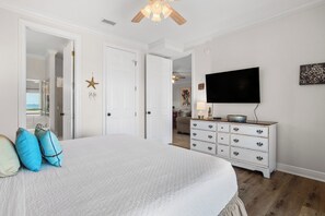 Quarto com cama, penteadeira, televisão e porta que dá para outro espaço.