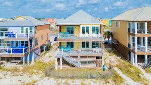 A beachfront property with multiple levels, outdoor seating, and a staircase leading to the upper floors. - Beachfront Bliss | Heated Private Pool | Pet Friendly (Gulf Shores)