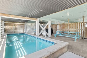 An indoor swimming pool with a wooden deck area, a diving board, and a safety sign.
