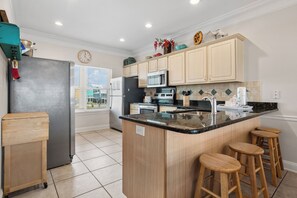 A modern kitchen with a central island, bar stools, and a view to the outside.