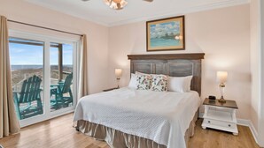 A bedroom with a large bed, a ceiling fan, a painting, and a view through a sliding glass door. - Beachfront Bliss | Heated Private Pool | Pet Friendly (Gulf Shores)