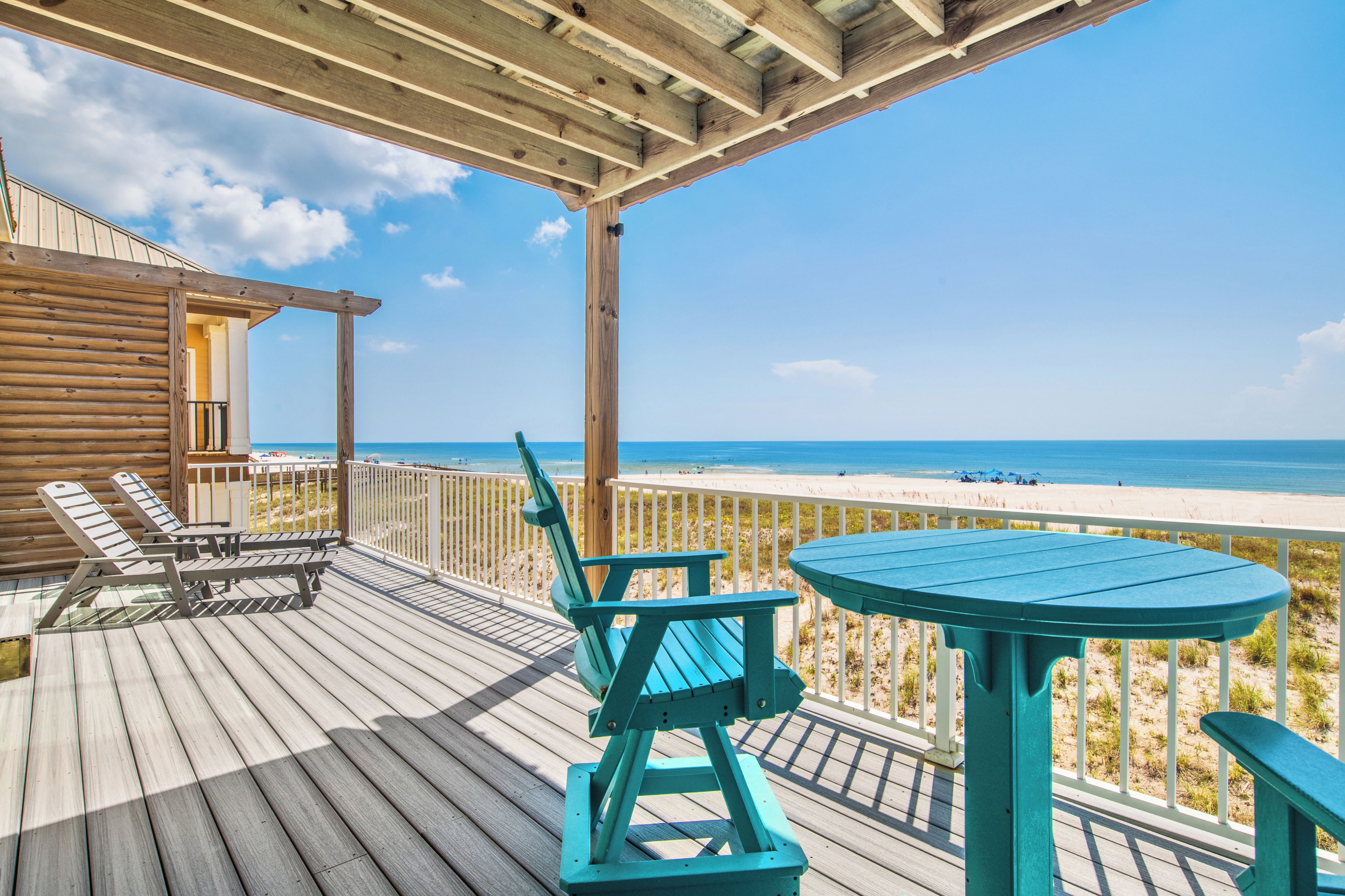 A wooden deck with outdoor furniture overlooking a beach.