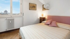 Una camera da letto con una grande finestra, un letto con lenzuola a righe, un comodino con una lampada e due quadri appesi al muro.