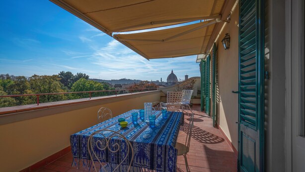 Un balcone con tavolo e sedie, vista su un edificio con una cupola e pavimento piastrellato.