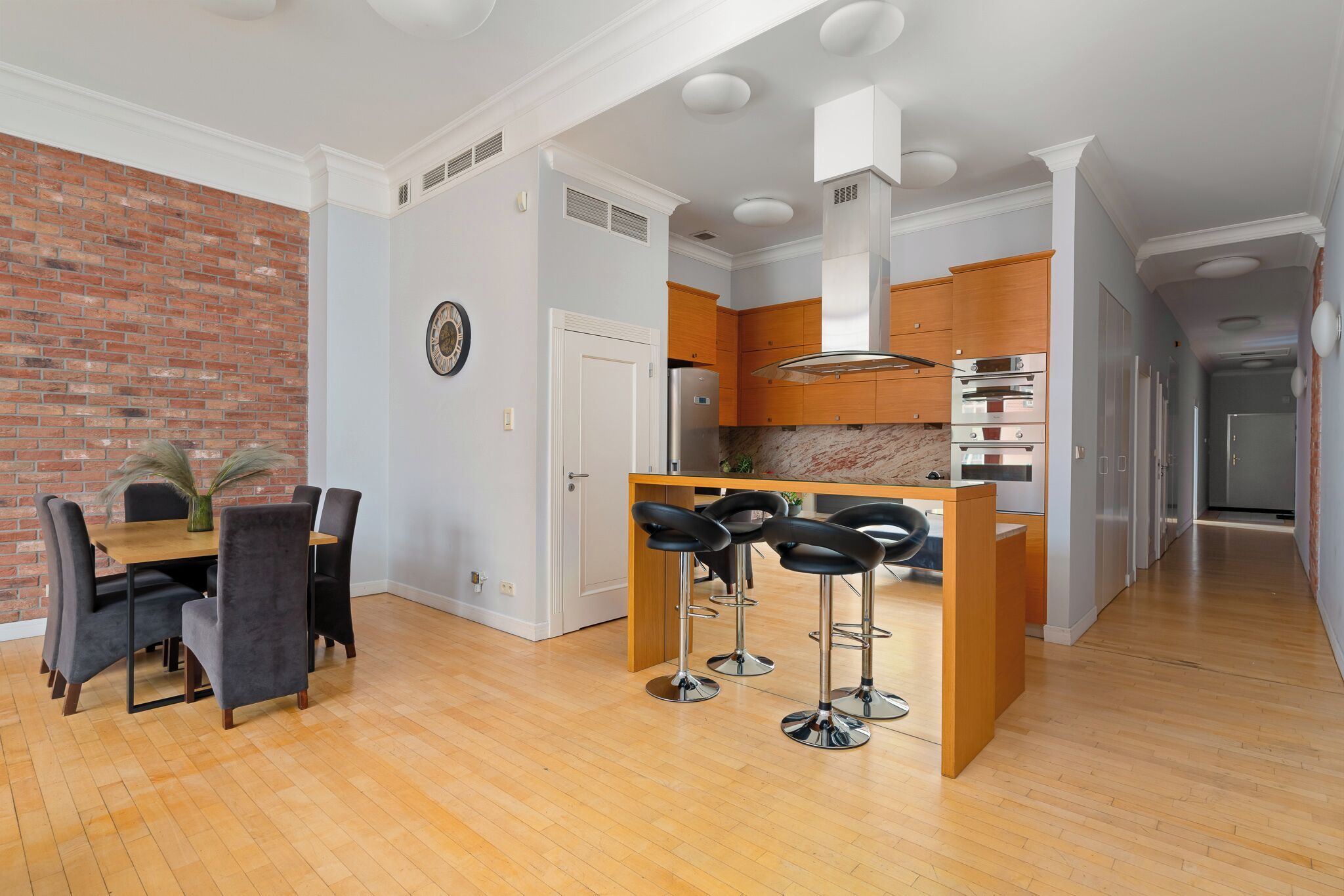 A modern kitchen with wooden cabinets, a central island with bar stools, and a brick accent wall.
