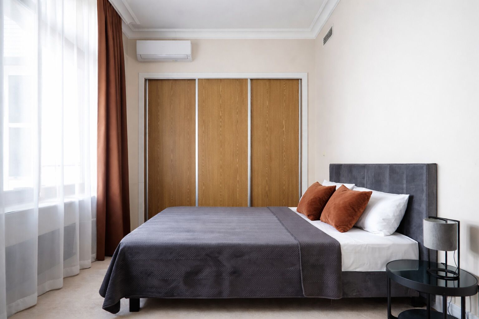 A bedroom with a bed, a wardrobe, a bedside table, and a lamp.