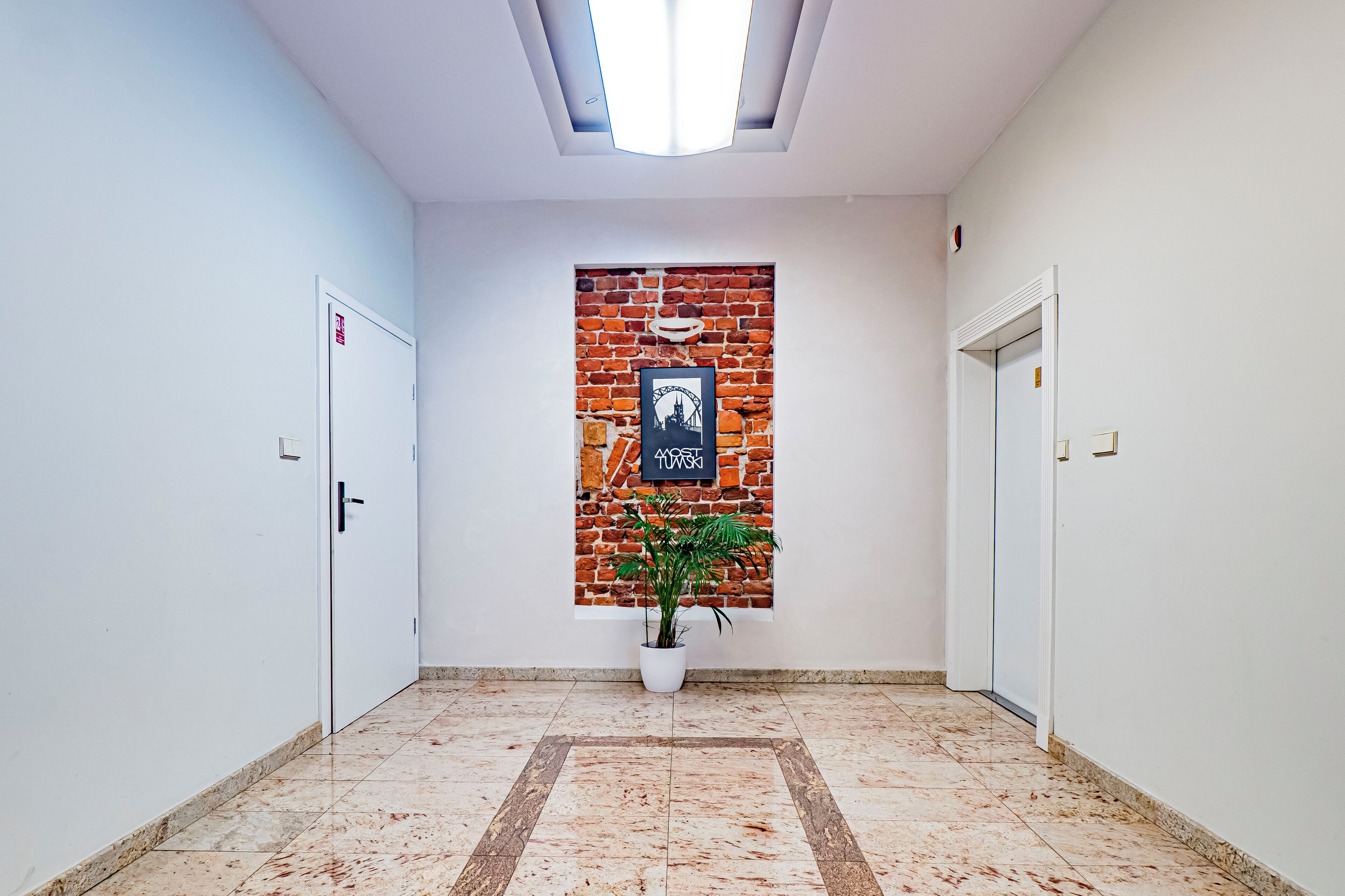 A hallway with white walls, a brick accent wall, a potted plant, and a framed picture.
