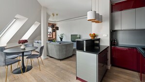 A modern kitchen with a central island, red cabinets, and a dining area with a round table and chairs. - AS HOME Apartamenty Rynek 50 (Wroclaw)