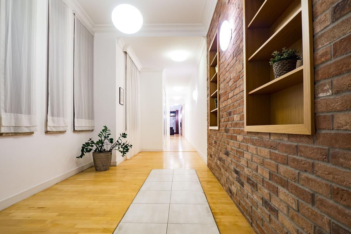A hallway with a wooden floor, white walls, and a brick accent wall with shelves.
