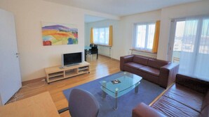 A living room with a glass coffee table, a brown sofa, a TV on a stand, and a painting on the wall. - Tranquil Seafront Escape (Zürich)