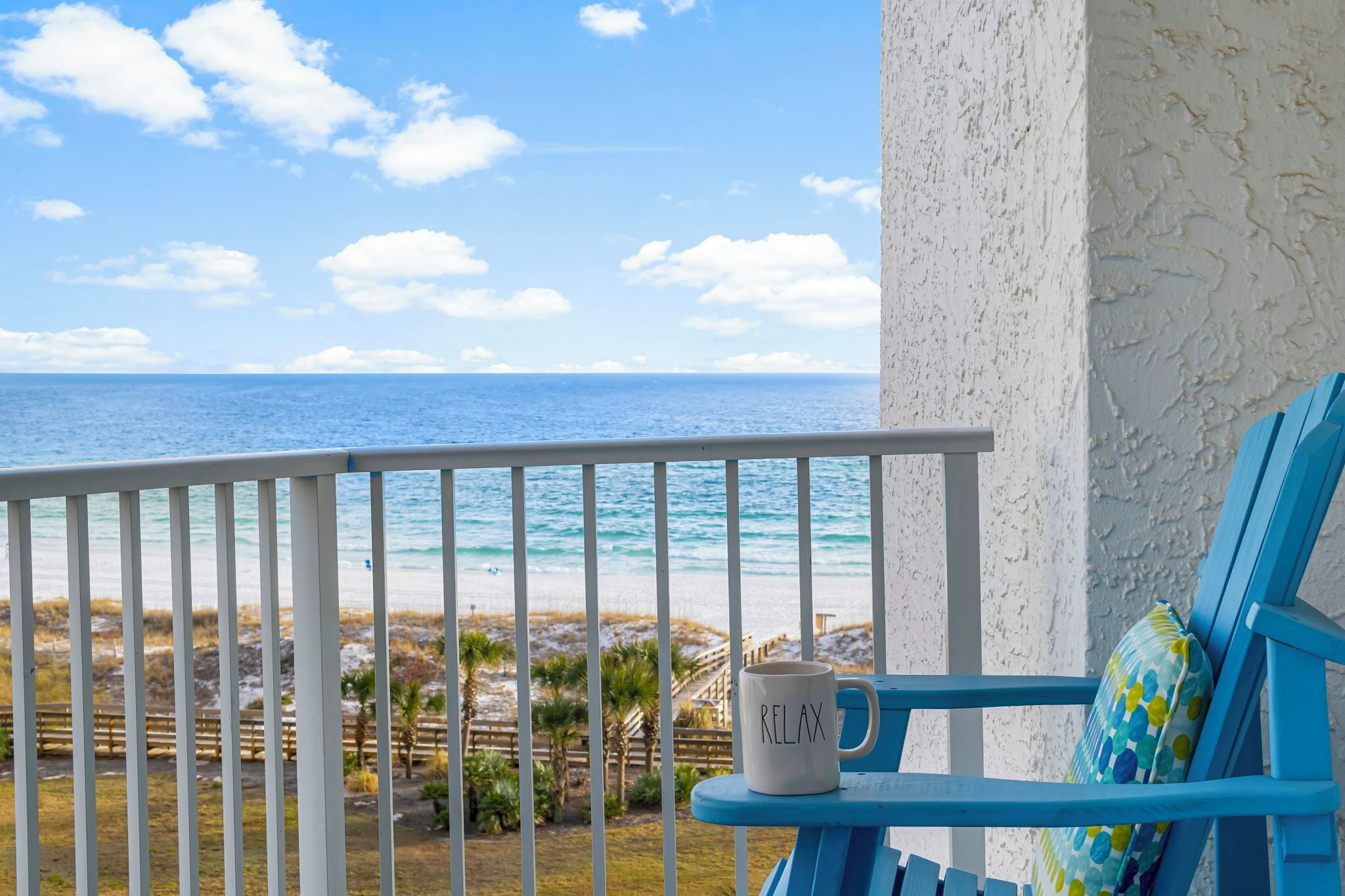 A balcony with a white railing, a blue chair, and a white mug with "RELAX" on it.