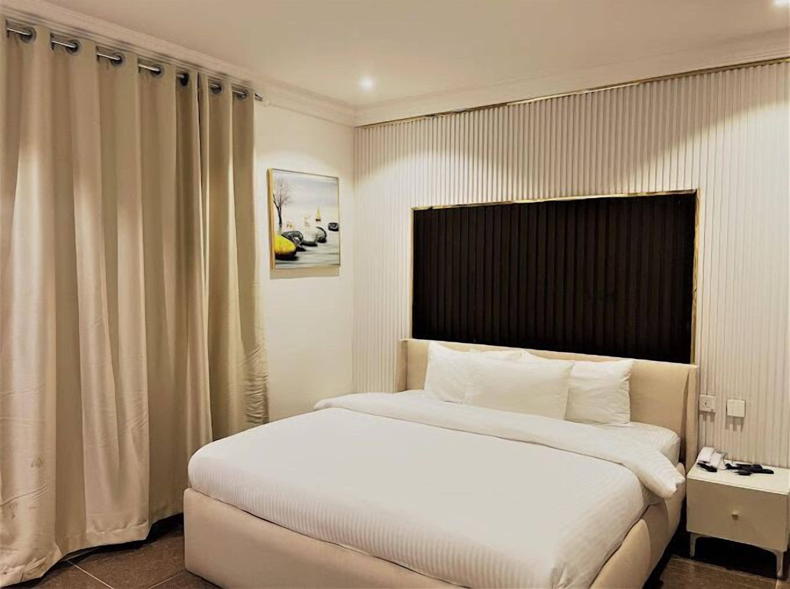 A hotel room with a large bed, a bedside table with a phone, and a painting on the wall.