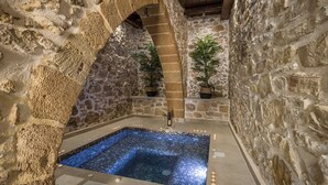 Un área de spa con paredes de piedra, una bañera de hidromasaje rectangular, plantas en macetas y velas.