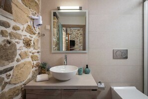 A bathroom with a stone wall, a white sink, a mirror, and a shower area.