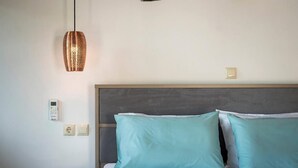 Una cama bien hecha con almohadas azul claro, una mesita de noche con una tableta, un termostato en la pared y una lámpara colgante.