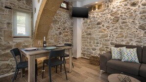 Una habitación acogedora con pared de piedra, una mesa de comedor de madera con sillas, un televisor de pantalla plana en la pared y un sofá marrón con cojines estampados.