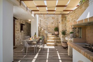Un patio con paredes de piedra, una mesa y sillas, una escalera y plantas en macetas.