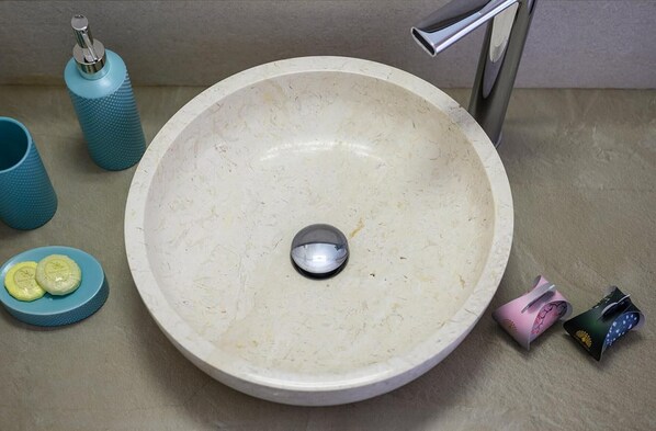 Un lavamanos con un lavabo redondo, un grifo, un porta cepillos de dientes y un jabonera.