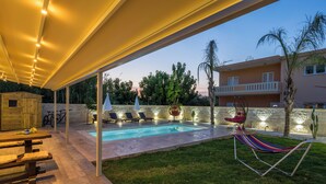 A covered outdoor area with a pool, lounge chairs, a hammock, and a dining table. - Garden Villa - bikes, private pool, garden family home (Crete)