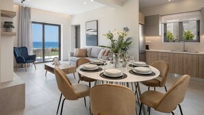 A modern dining area with a round table set for six, a sofa, and a view of the sea. - GG Villas Falassarna (Chania)